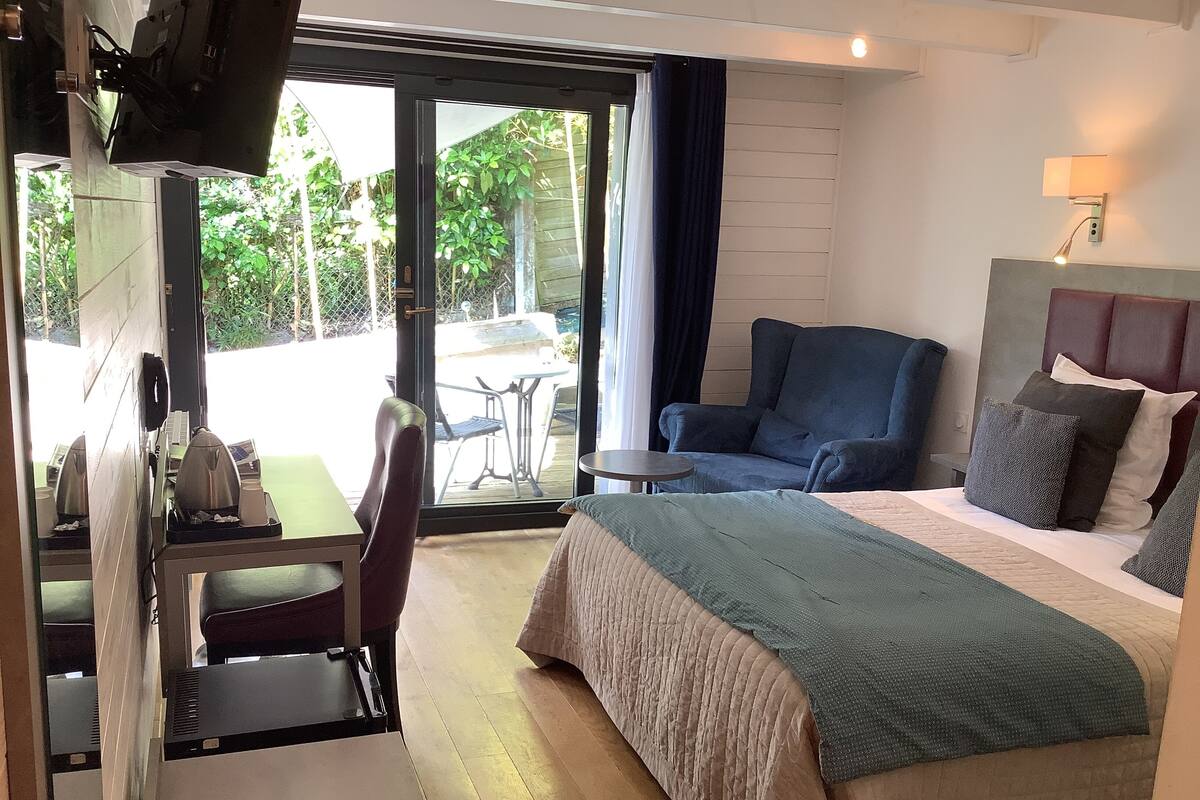 Habitación de hotel con cama, escritorio y silla. Se ve vegetación por la ventana.