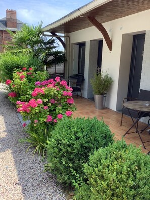 A patio area with a table and chairs, surrounded by lush greenery and flowering plants. - Hôtel Monet (Honfleur)