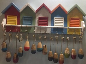 A row of colorful miniature houses with keys hanging from a rack. - Hôtel Monet (Honfleur)