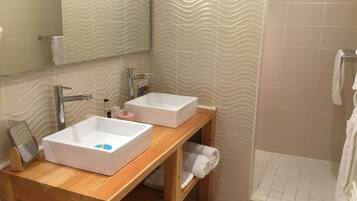 A bathroom with two white sinks, a wooden vanity, a mirror, a towel rack, and a shower area.
