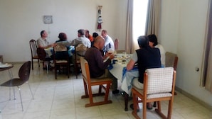 Un comedor con una mesa redonda y sillas, un reloj en la pared y una ventana con cortinas.