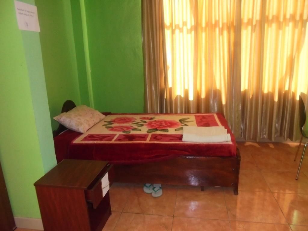 A room with a bed, a small table, and a pair of slippers on the floor.
