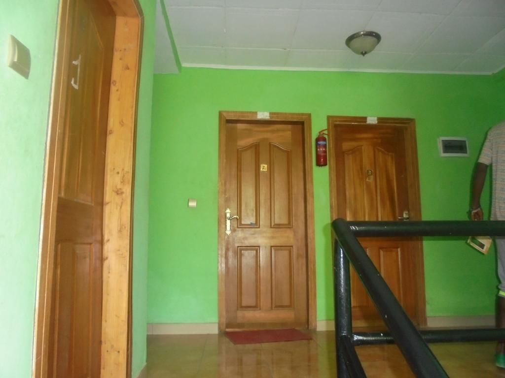 Un pasillo con paredes verdes, puertas de madera y barandal negro.