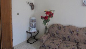 Una sala de estar con un sofá floral, una mesita con dispensador de agua y un jarrón con flores rojas.