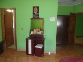 Una habitación con una pared verde, un escritorio de madera con un espejo, un banco pequeño y una cama con una colcha de diseño rojo y negro.