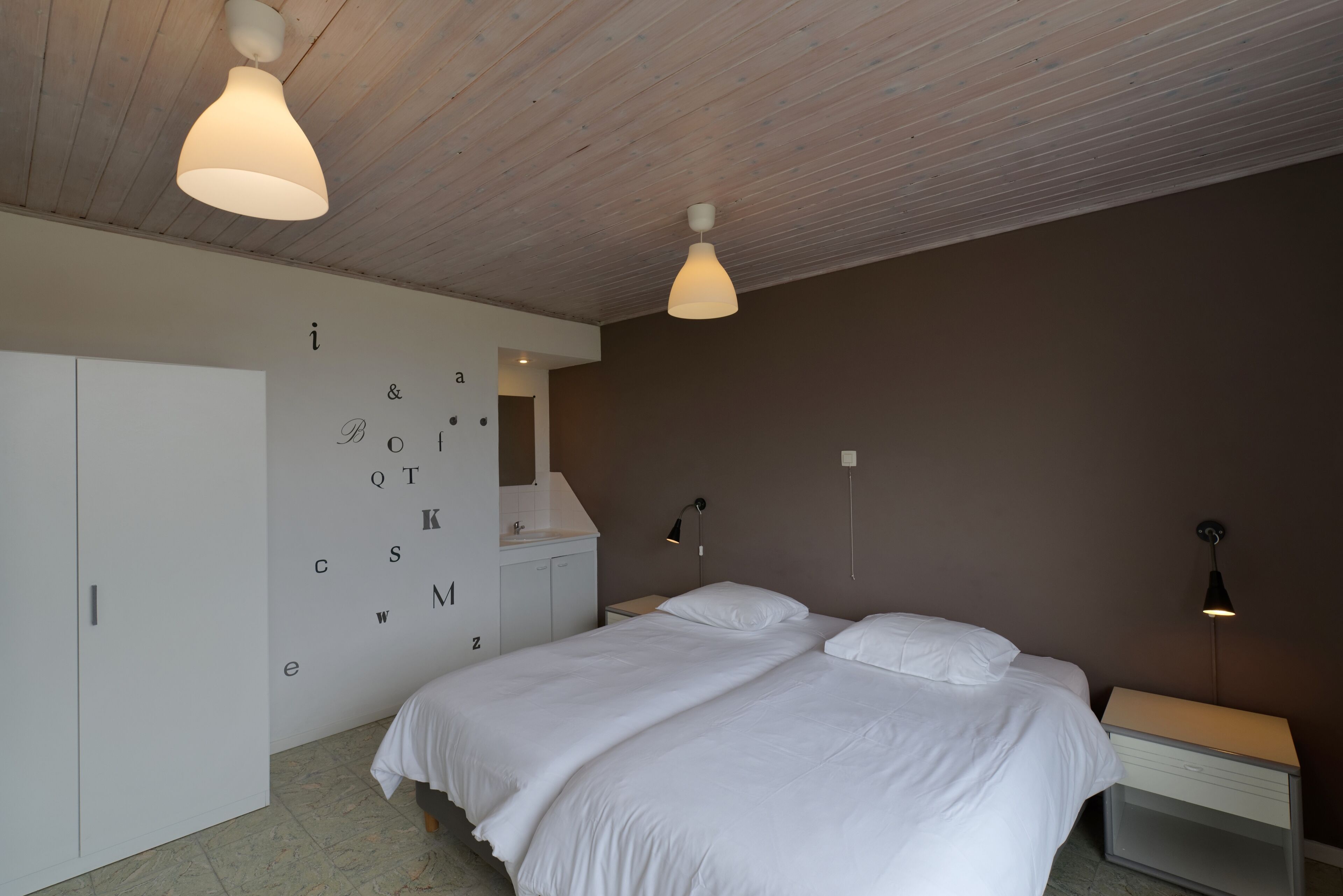 Une chambre à coucher comprenant un lit, des tables de chevet, une armoire et un mur orné de lettres.