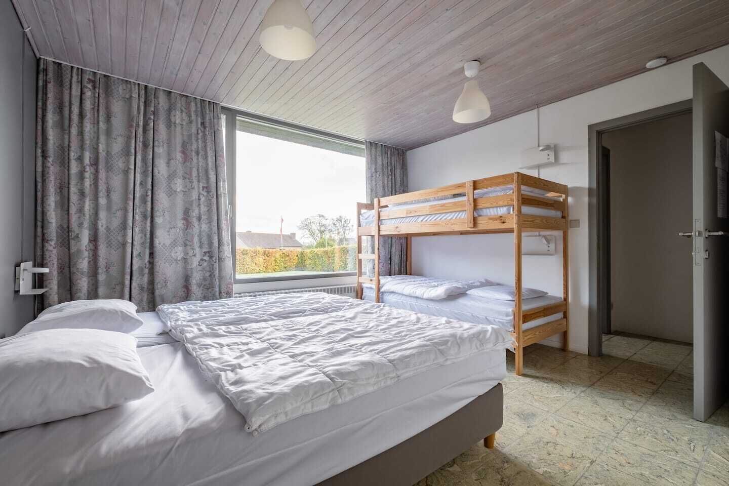 Une chambre avec un grand lit, un lit superposé, une fenêtre avec des rideaux et une porte.