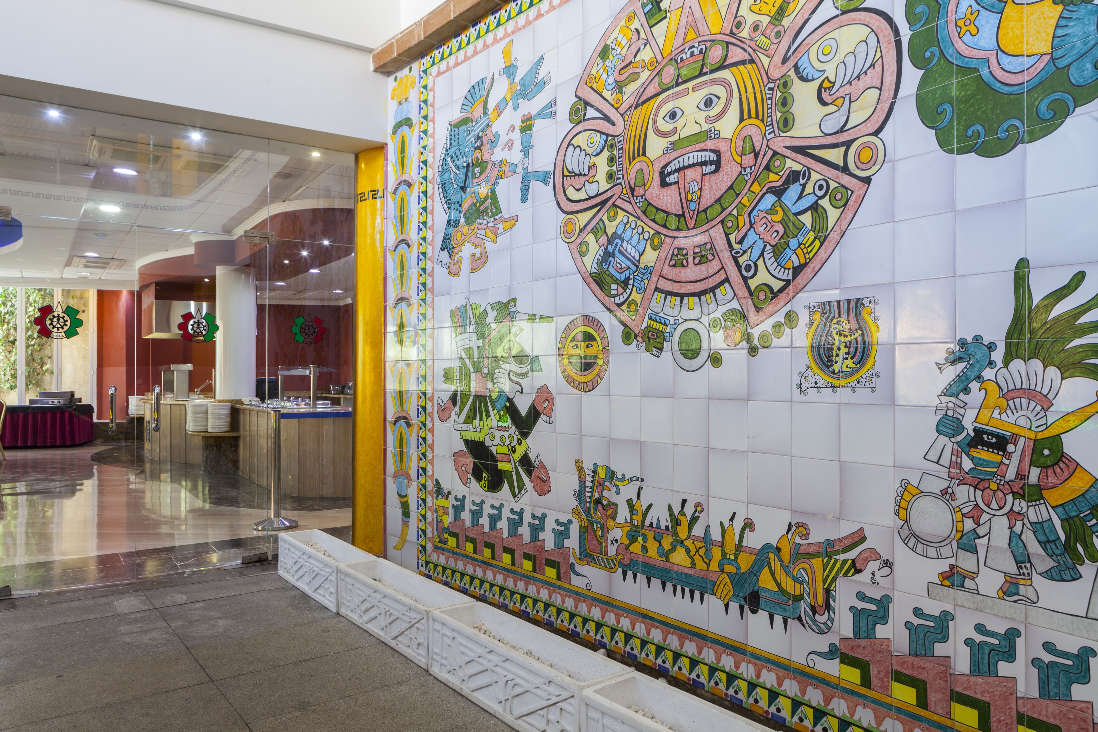 Un vestíbulo con un gran mural colorido que representa diseños y figuras de la antigua civilización azteca.