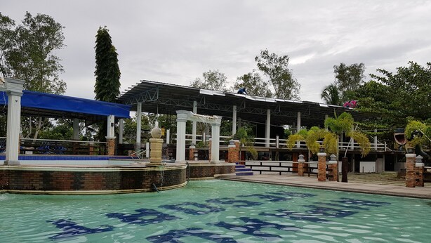 Una piscina con una fuente, rodeada por una zona techada con columnas y un techo azul.
