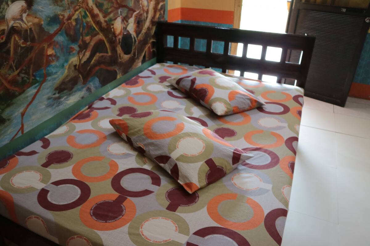 A bed with a colorful circular pattern bedspread and matching pillows, a black headboard, and a mural on the wall.