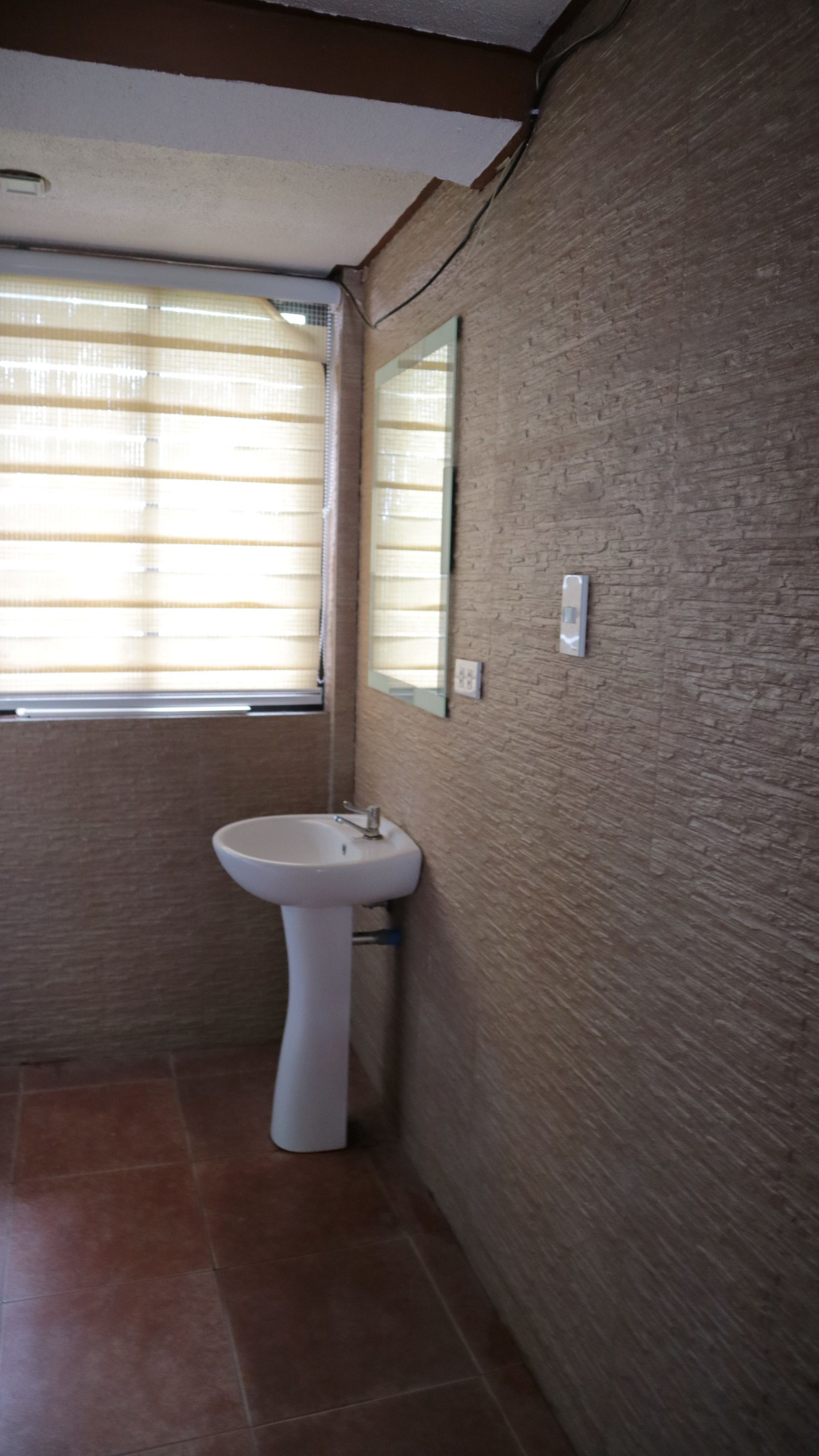 Un baño con un lavabo blanco, una ventana con persianas y una pared con textura.
