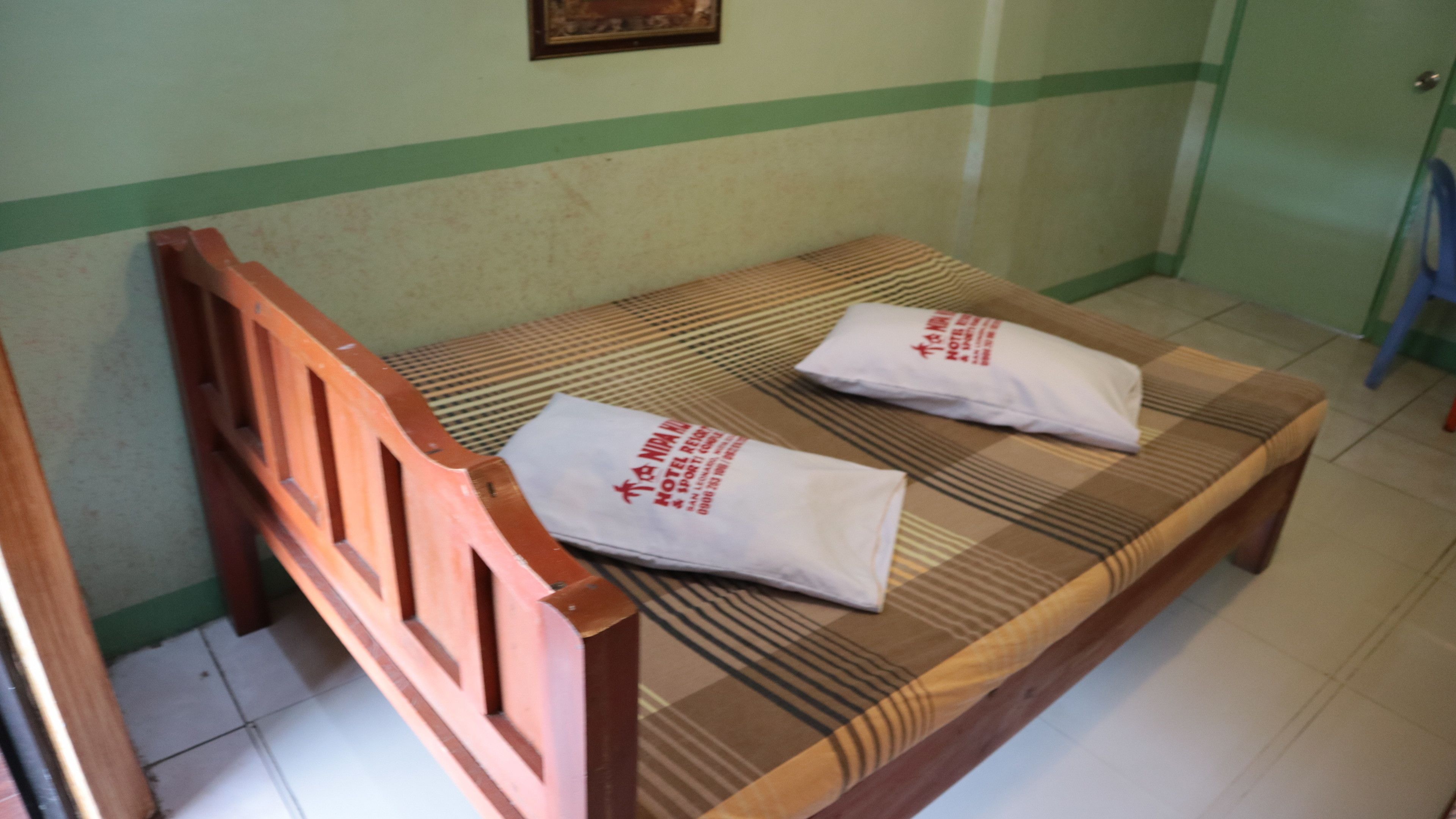 Una cama individual con cabecera de madera y dos almohadas blancas con texto estampado.