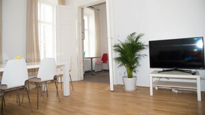 A modern living room with a flat-screen TV, a potted plant, and a dining area with chairs and a table. - Vienna Hotspot - Museum (Vienna)