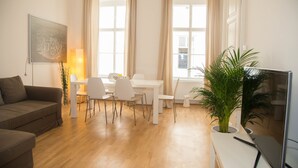 A modern living room with a brown sofa, a dining table with four chairs, a TV, and a potted plant. - Vienna Hotspot - Museum (Vienna)