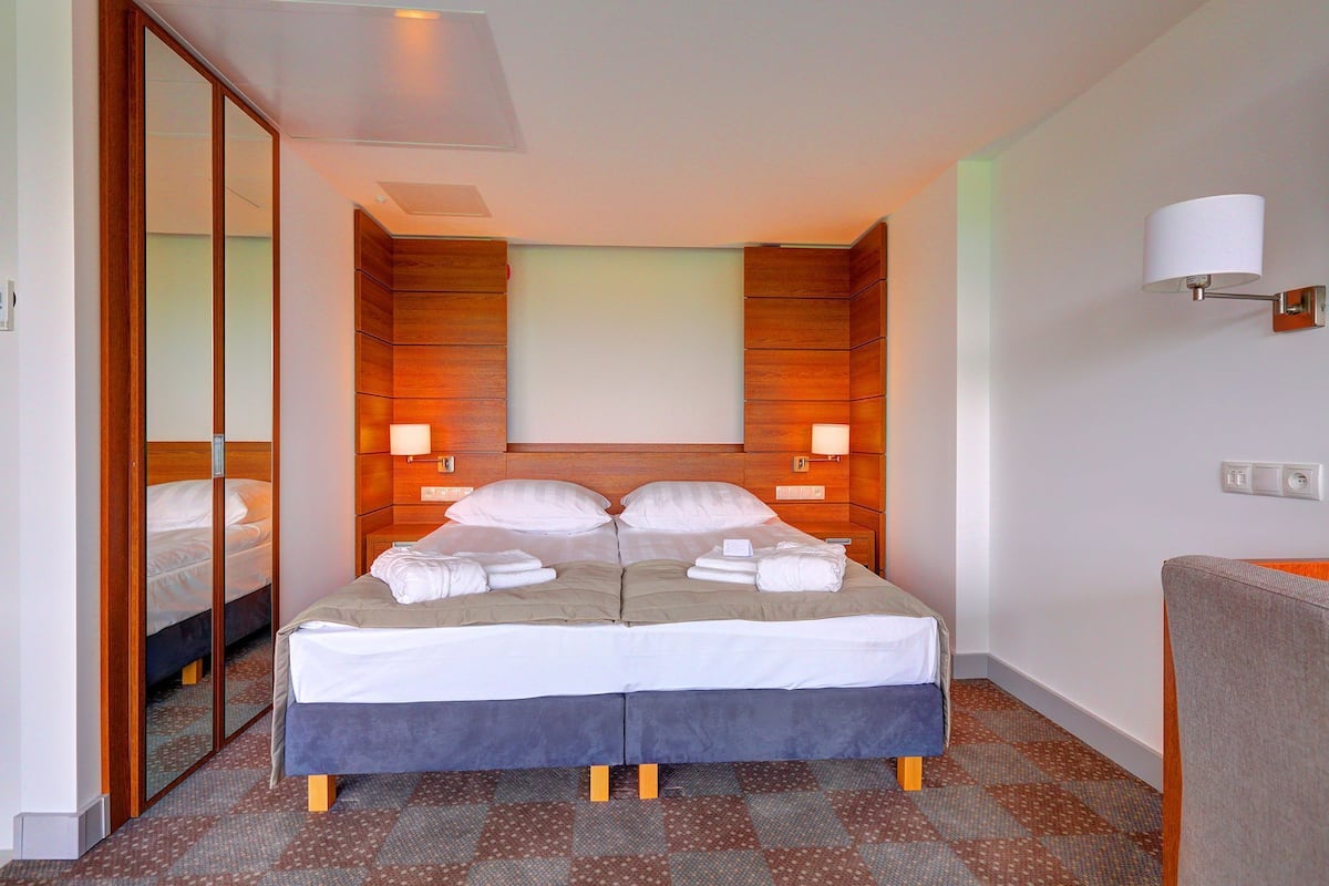 Ein Hotelzimmer mit einem großen Bett, einem Spiegel, einem Nachttisch, einer Lampe und einem Sessel.