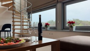 Een moderne kamer met een wenteltrap, een eettafel met fruit en wijnglazen, en uitzicht op het omliggende landschap door grote ramen.