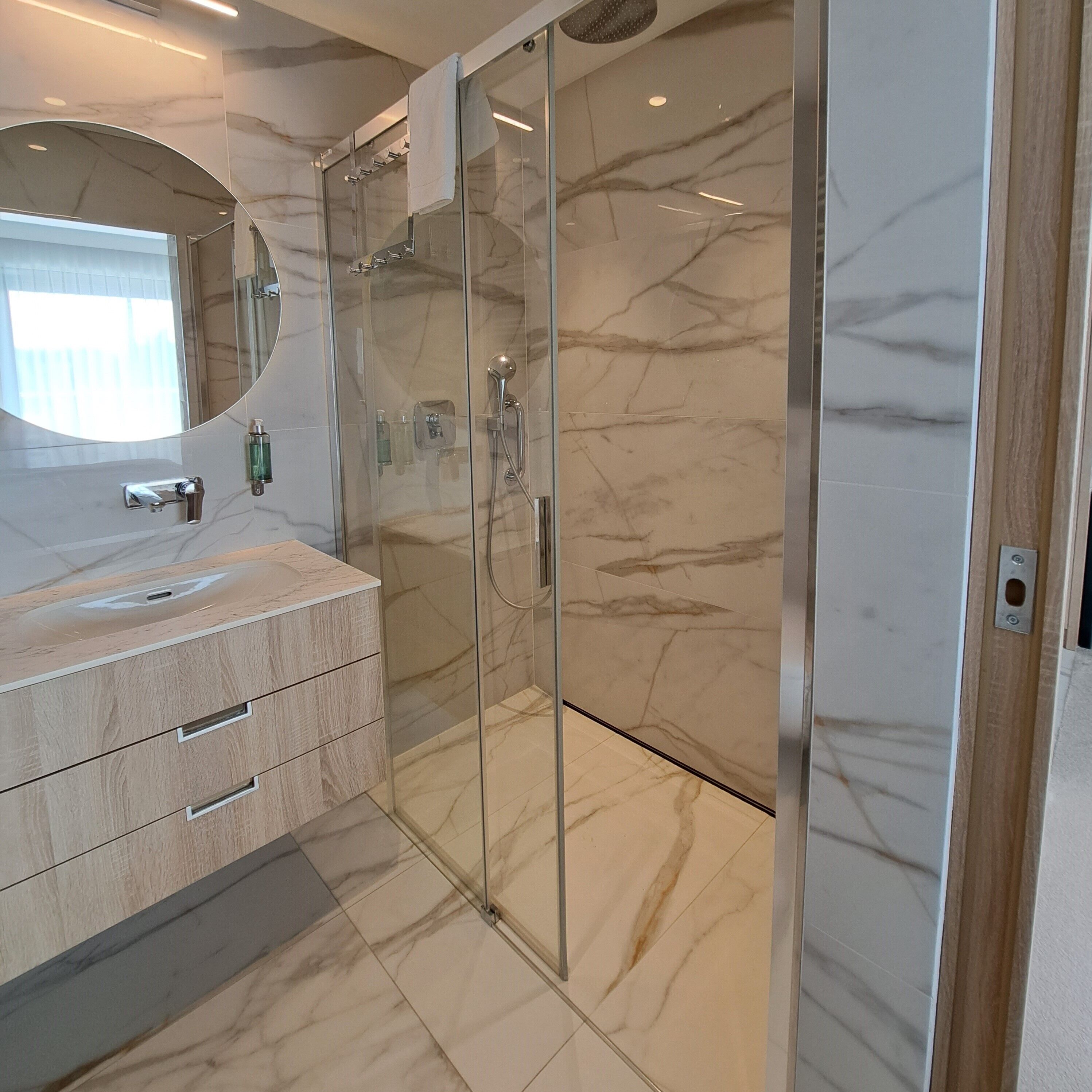 A modern bathroom with a glass-enclosed shower, a marble-tiled floor, and a vanity with a mirror.