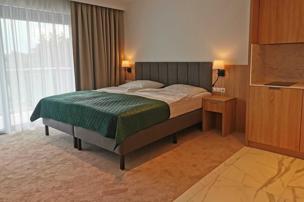 Ein modernes Hotelzimmer mit einem Bett, einem Holzschrank und einem Nachttisch mit Lampe.
