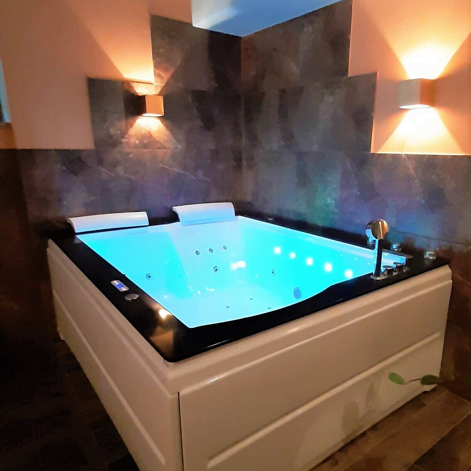 Un moderno jacuzzi con control digital, rodeado por un diseño minimalista con paredes de piedra e iluminación integrada.