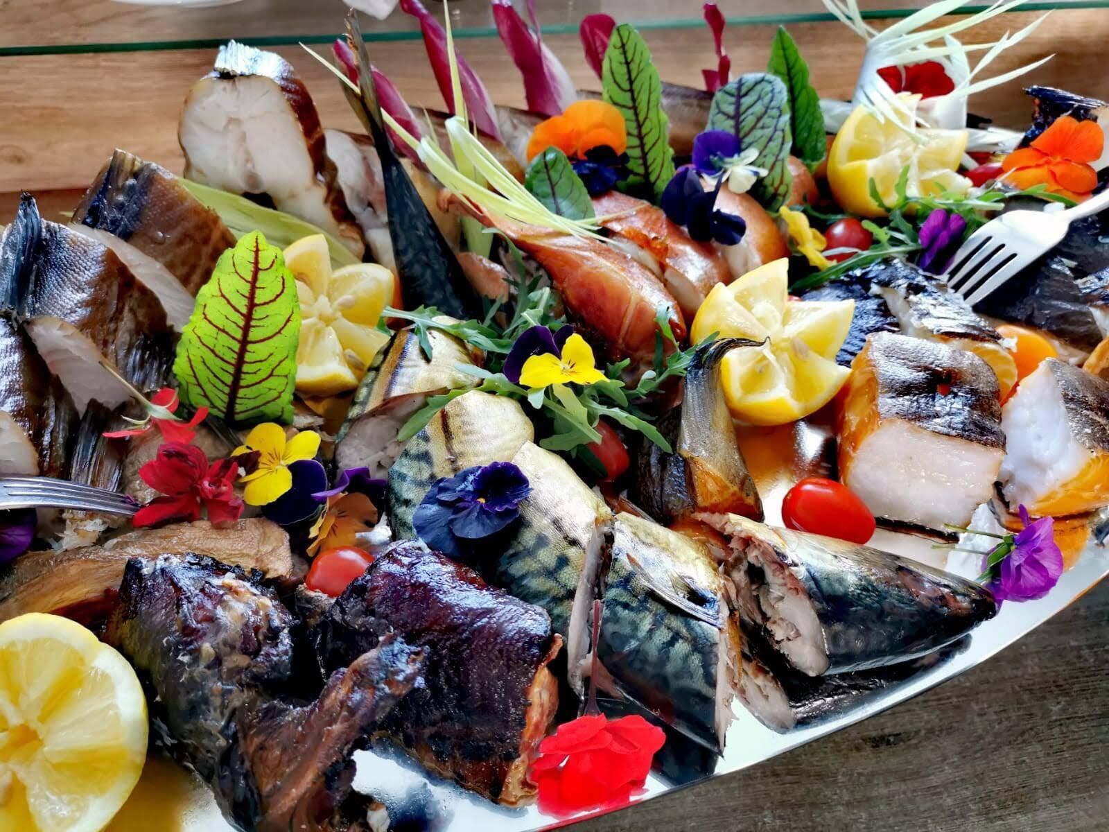 A platter of various fish and seafood, garnished with flowers and lemon slices.