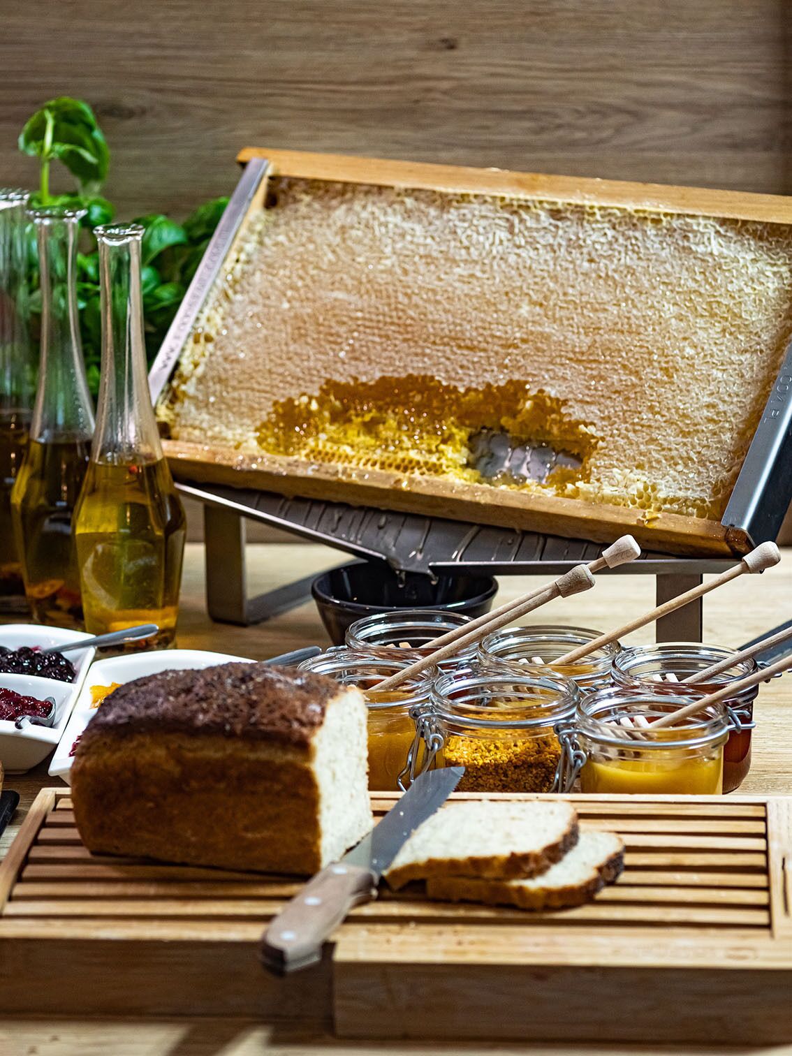 Una mesa de madera con un marco de panal, tarros de miel, hogaza de pan y un cuchillo.
