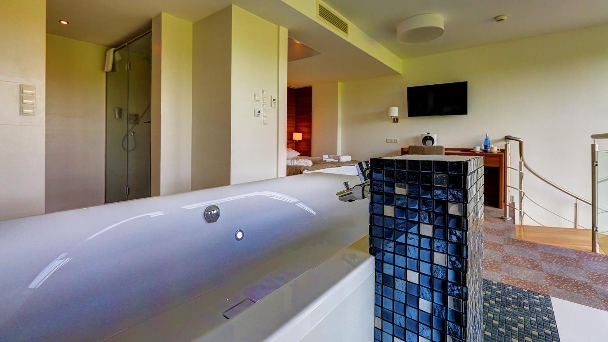 Une salle de bain moderne dotée d’une grande baignoire, d’un espace douche et d’un téléviseur fixé au mur.
