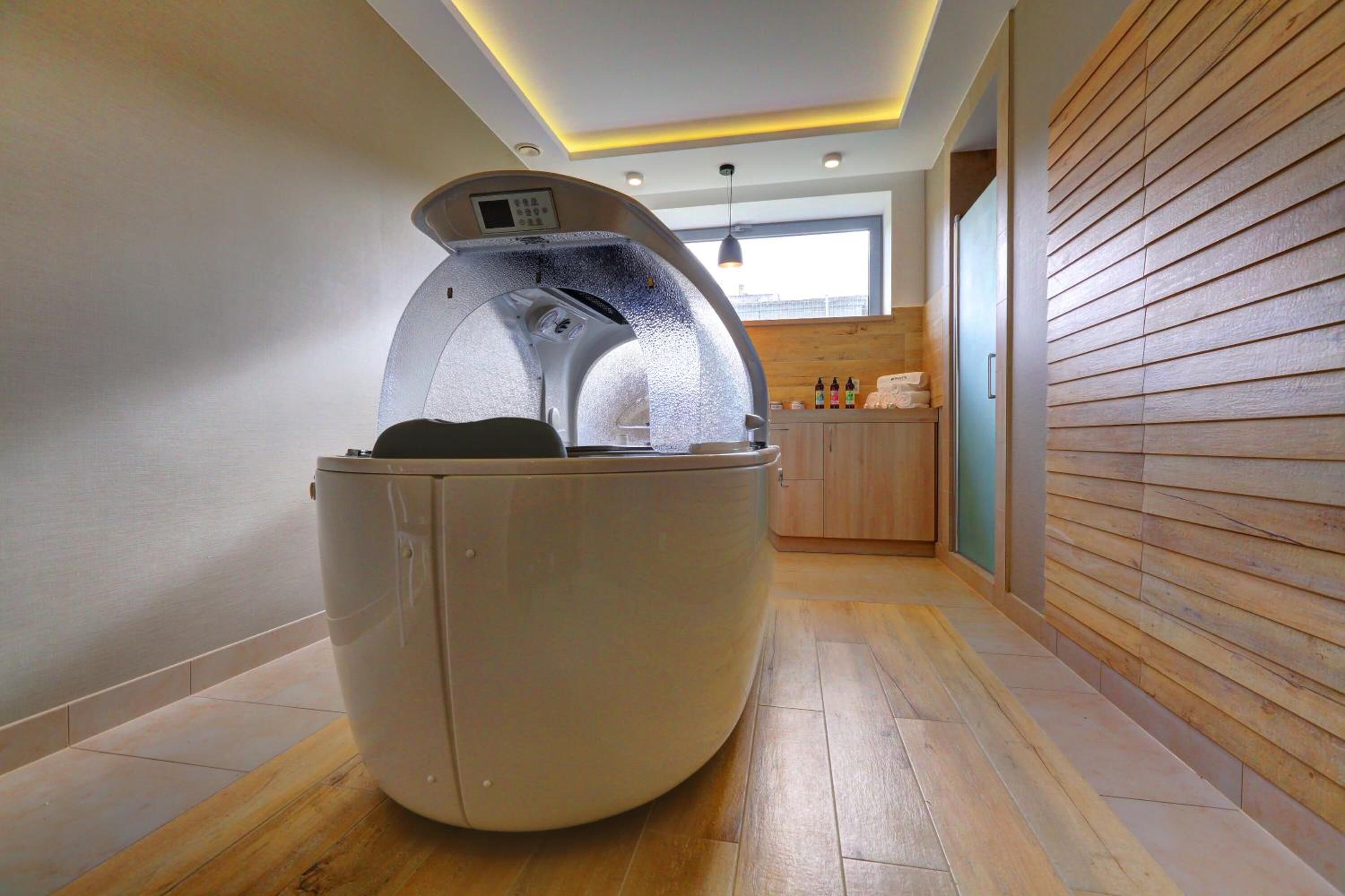 A modern spa room with a steam sauna, wooden flooring, and a view of the city through a window.