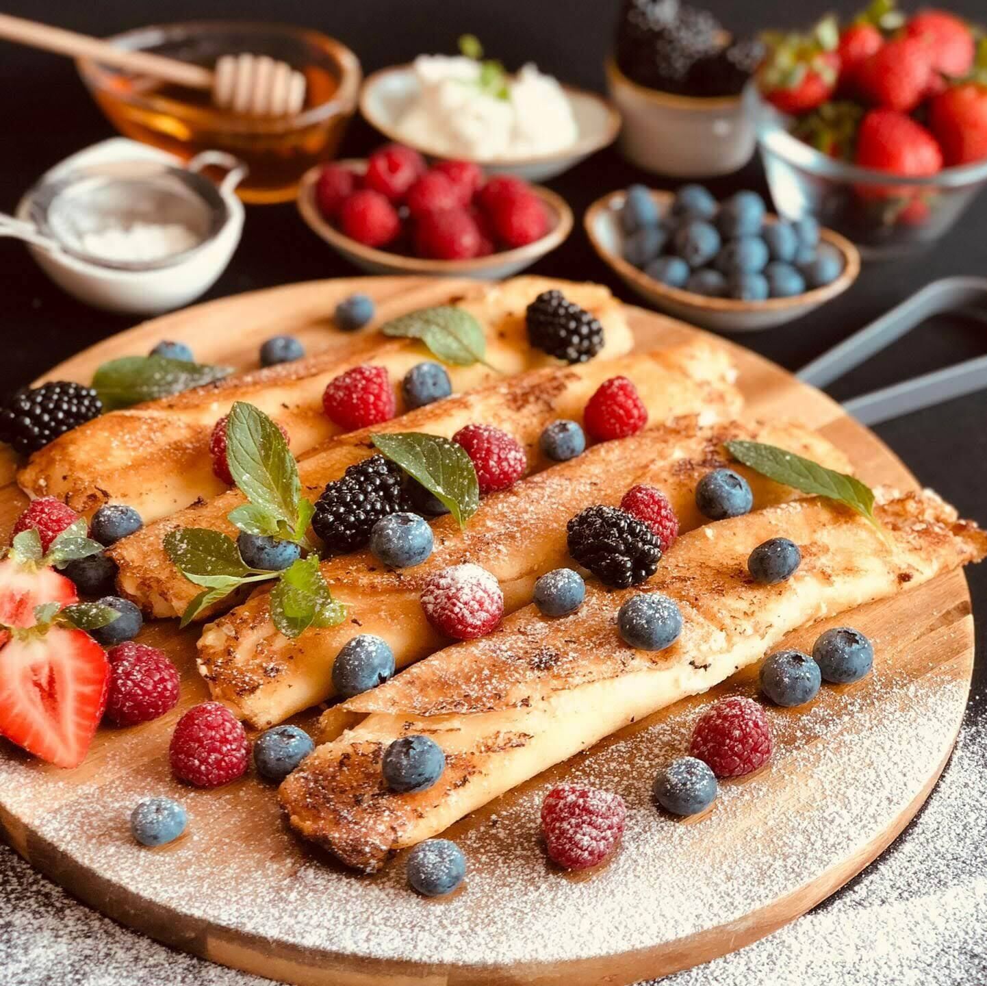 Une planche en bois sur laquelle sont disposées des crêpes garnies de fruits rouges et saupoudrées de sucre glace.