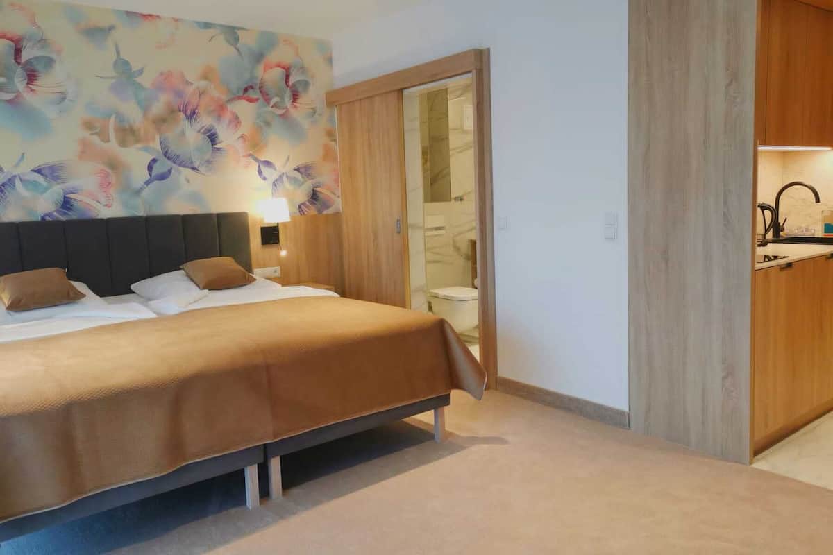 Ein modernes Hotelzimmer mit einem großen Bett, einem Holz-Kopfteil, Wandmalerei, einem Badezimmer mit Glastür und einer Küchenzeile.
