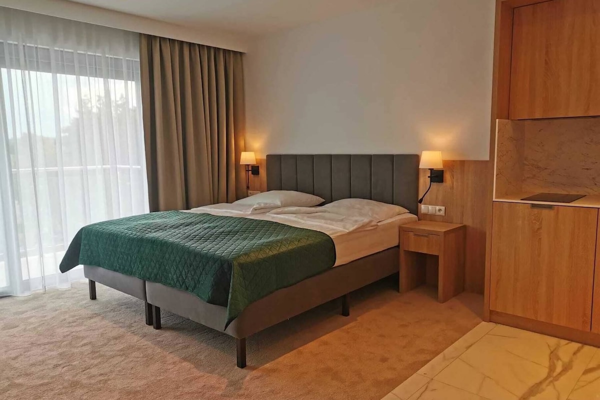 Une chambre d’hôtel avec un lit, deux lampes de chevet, une armoire en bois et une grande fenêtre avec des rideaux.