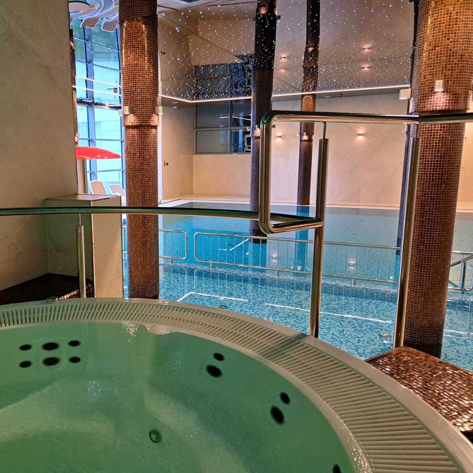 Een groot overdekt zwembad met een glazen afscheiding, een jacuzzi en uitzicht op het zwembad.