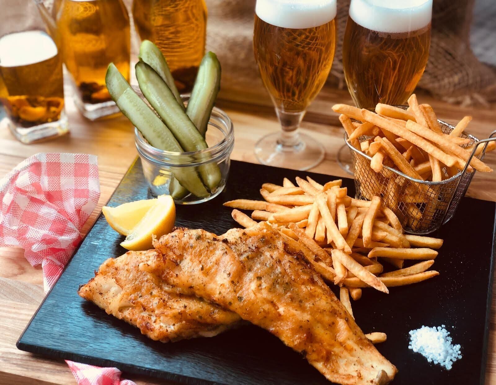 Un repas composé de poisson-frites, accompagné de cornichons, de citron et de verres à bière.