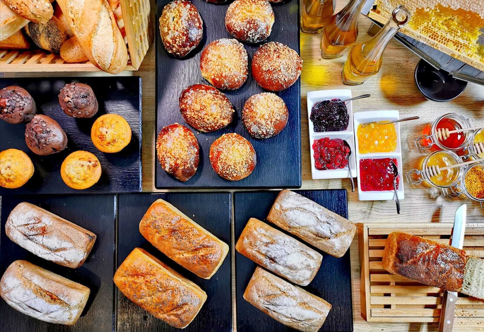 An assortment of baked goods including bread, muffins, and pastries, along with jars of honey and jams.