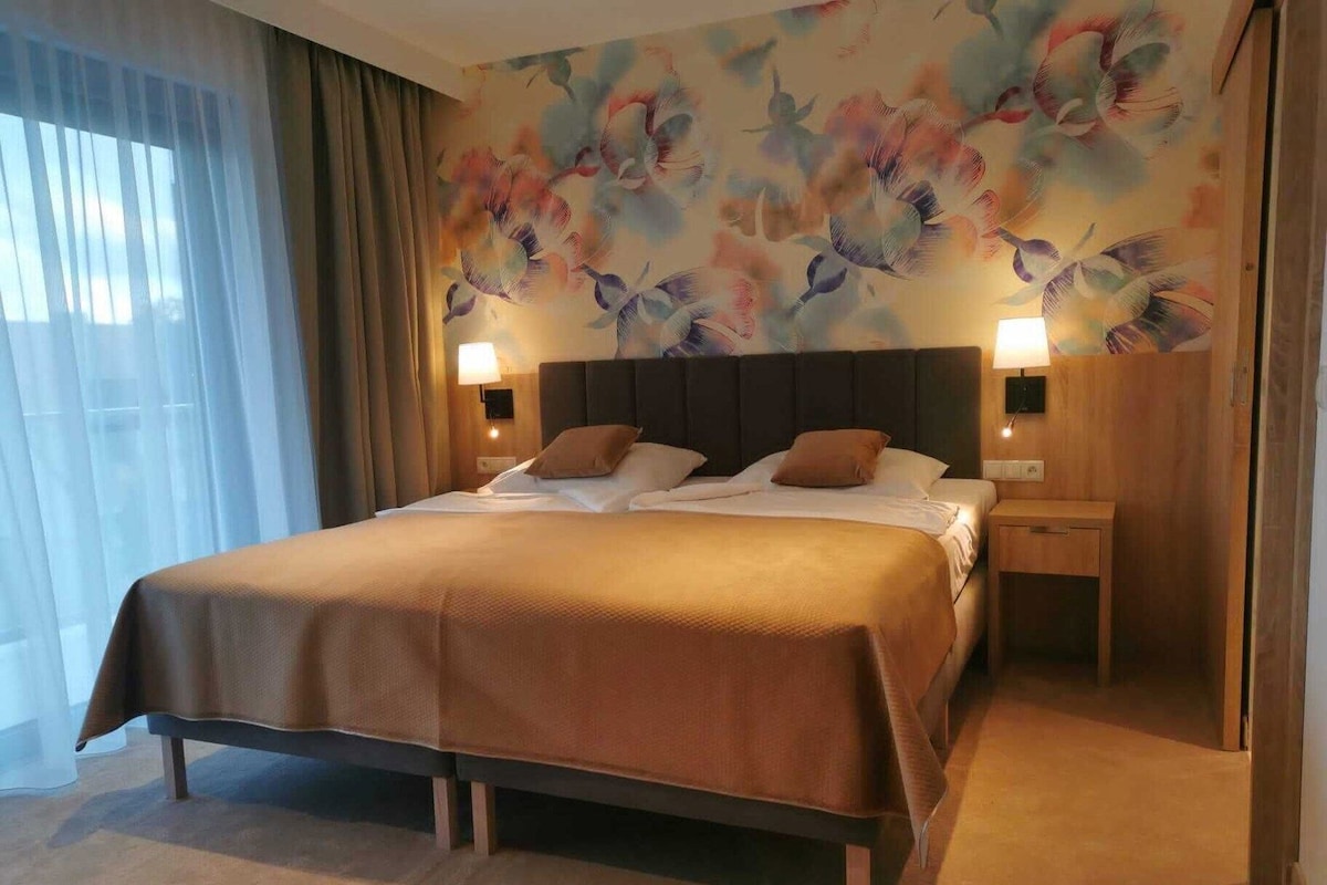 Une chambre d’hôtel avec un grand lit, deux tables de chevet, une tête de lit et une décoration murale à motifs floraux.