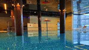 Een binnenzwembad met helderblauw water, metalen relingen en een glazen wand die het zwembad weerspiegelt.