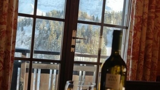 Une table avec deux verres à vin et une bouteille de vin, placée devant une fenêtre donnant sur des montagnes enneigées.