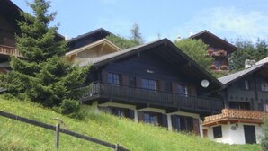 Un bâtiment de style chalet traditionnel, doté de nombreux balcons et entouré d’une végétation luxuriante et d’arbres.