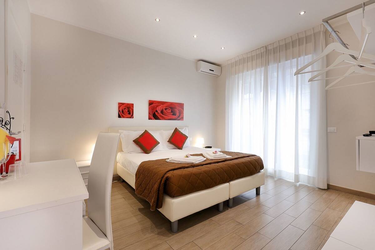 Una habitación de hotel moderna con una cama grande, muebles blancos y dos cuadros con rosas rojas en la pared.