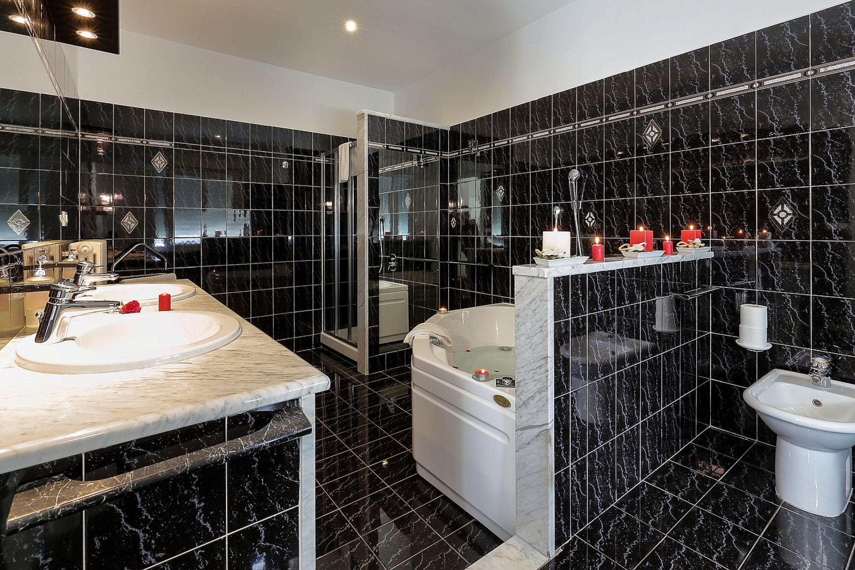 Une salle de bain moderne avec des carreaux de marbre noir, un double vasque, une baignoire et un bidet.