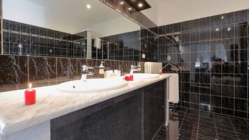A modern bathroom with two sinks, a large mirror, and black marble tiles.