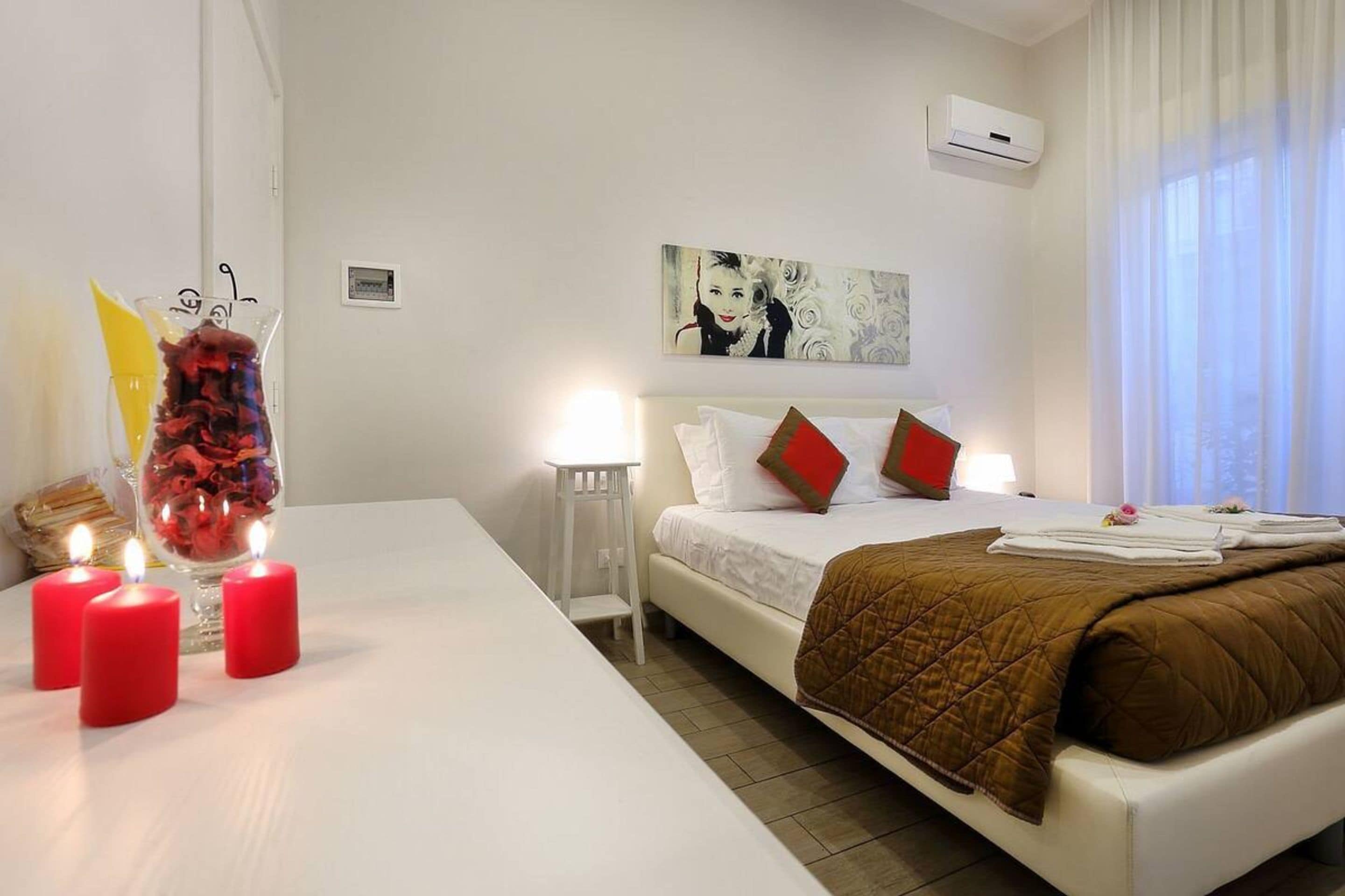 Une chambre d’hôtel avec un lit, des lampes de chevet, un tableau et un vase rempli de fleurs rouges.