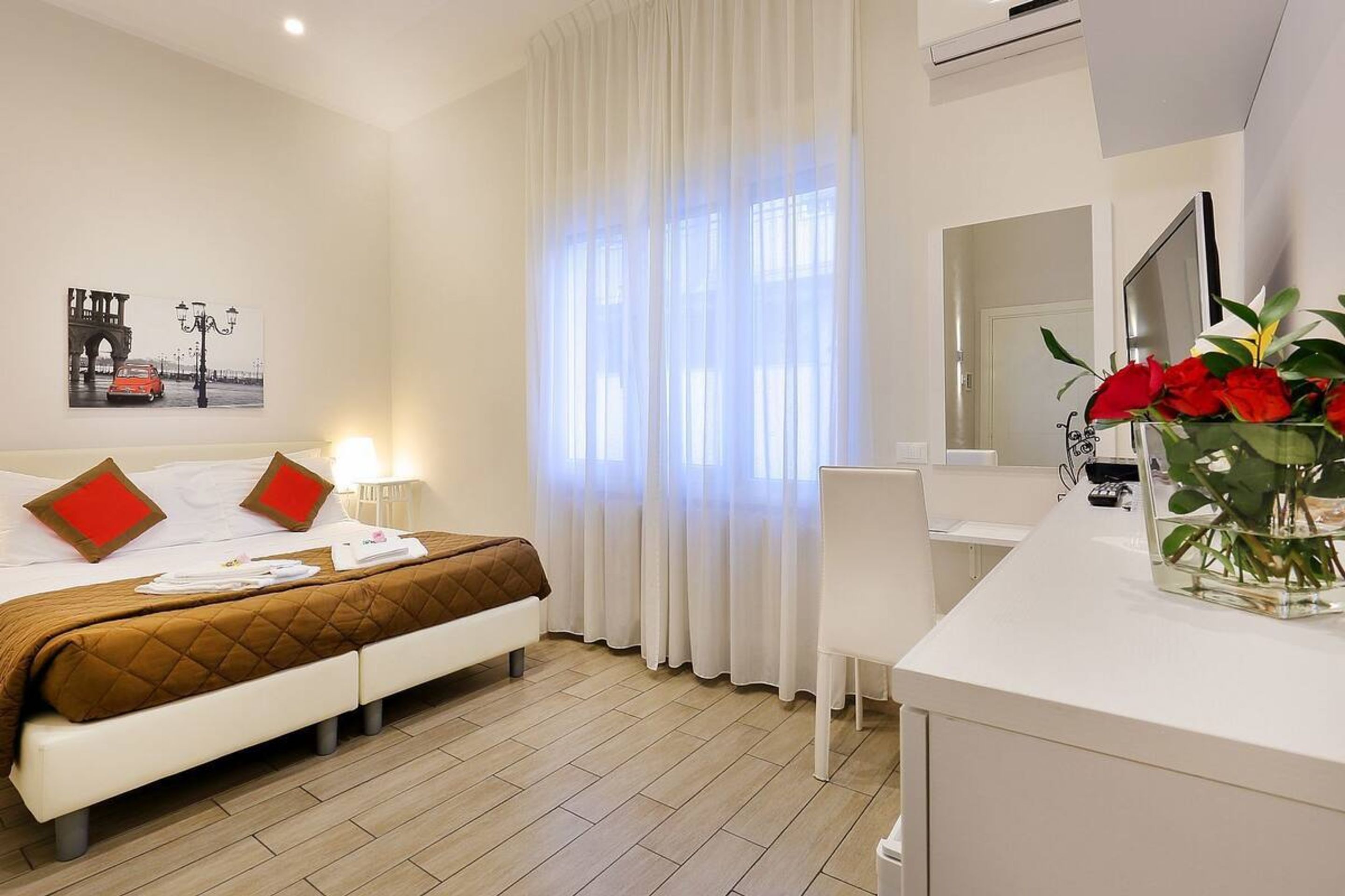 Ein Hotelzimmer mit Bett, Schreibtisch, Sessel, Fernseher und einem Fenster mit Vorhängen.