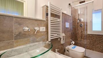 Un baño moderno con un lavamanos de vidrio, un inodoro blanco, una ducha con mampara de vidrio y un perchero para toallas.