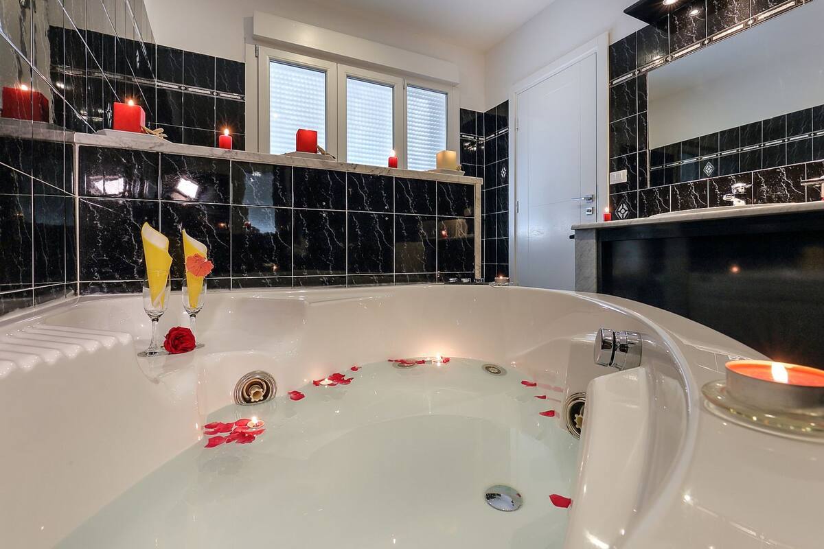 Un baño moderno con una bañera grande, baldosas de mármol negro y velas.