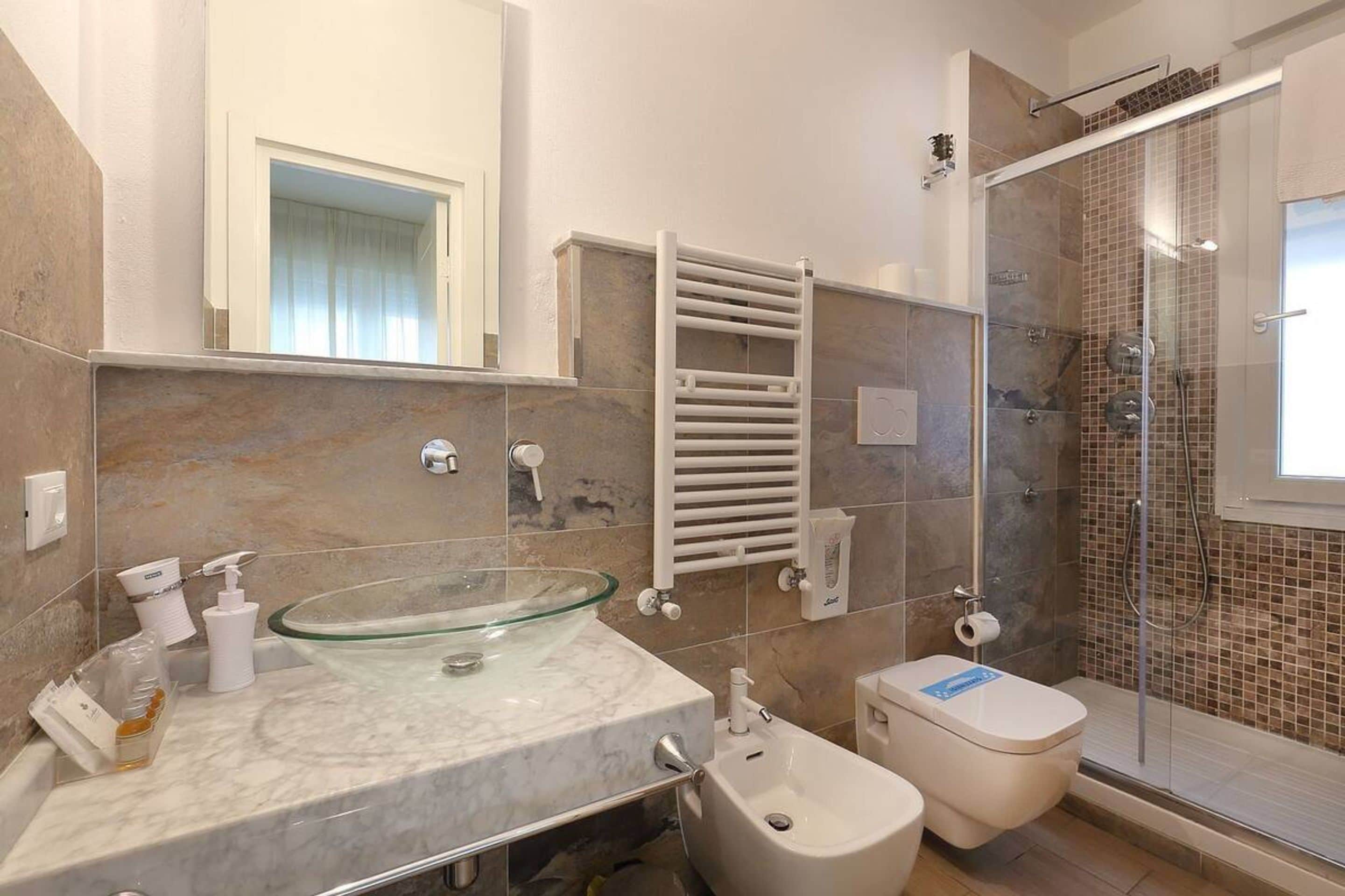 Une salle de bain moderne avec un lavabo en verre, un bidet, des toilettes, une douche avec des portes en verre et un porte-serviettes.