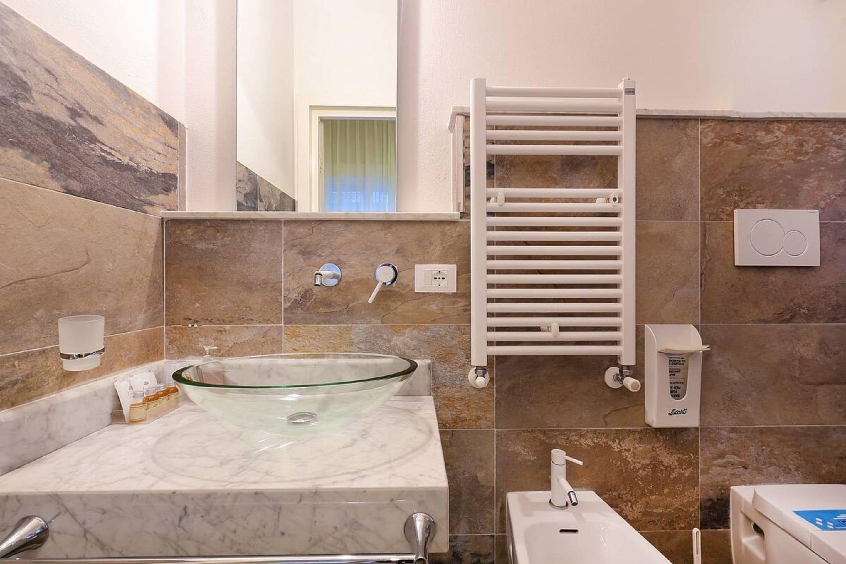A modern bathroom with a glass bowl sink, a white towel rack, and a handheld showerhead.