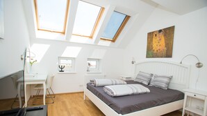 A bedroom with a bed, skylights, a desk, and a painting.