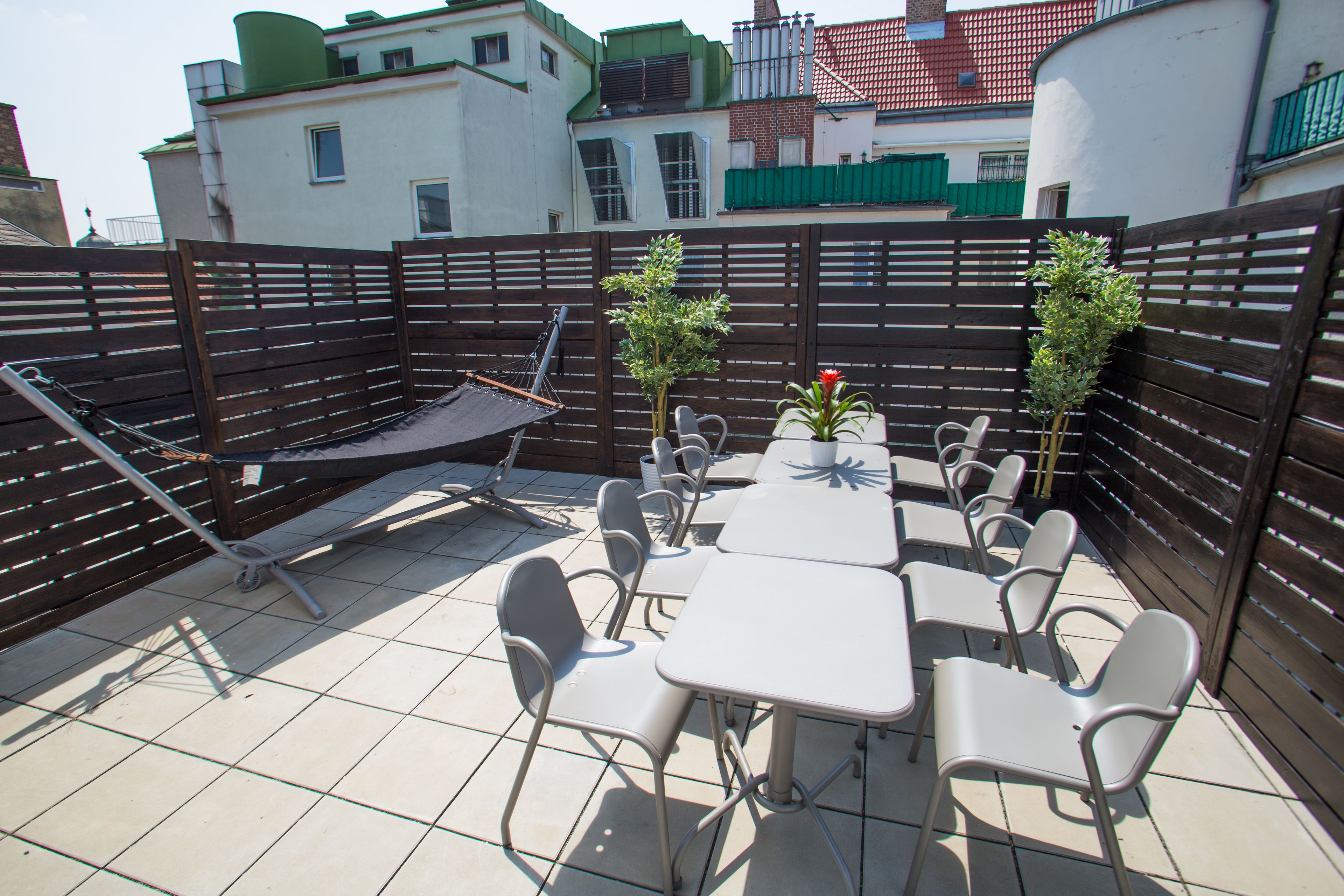 An outdoor patio with a table and chairs, a hammock, and a small garden area with two potted plants.