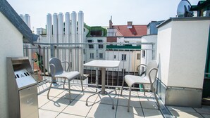 A rooftop terrace with a grill, two chairs, and a table.