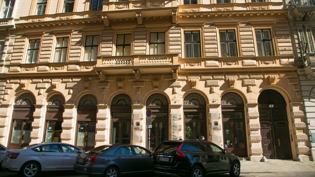 Un edificio storico con dettagli architettonici elaborati, diverse porte d'ingresso e una bandiera.
